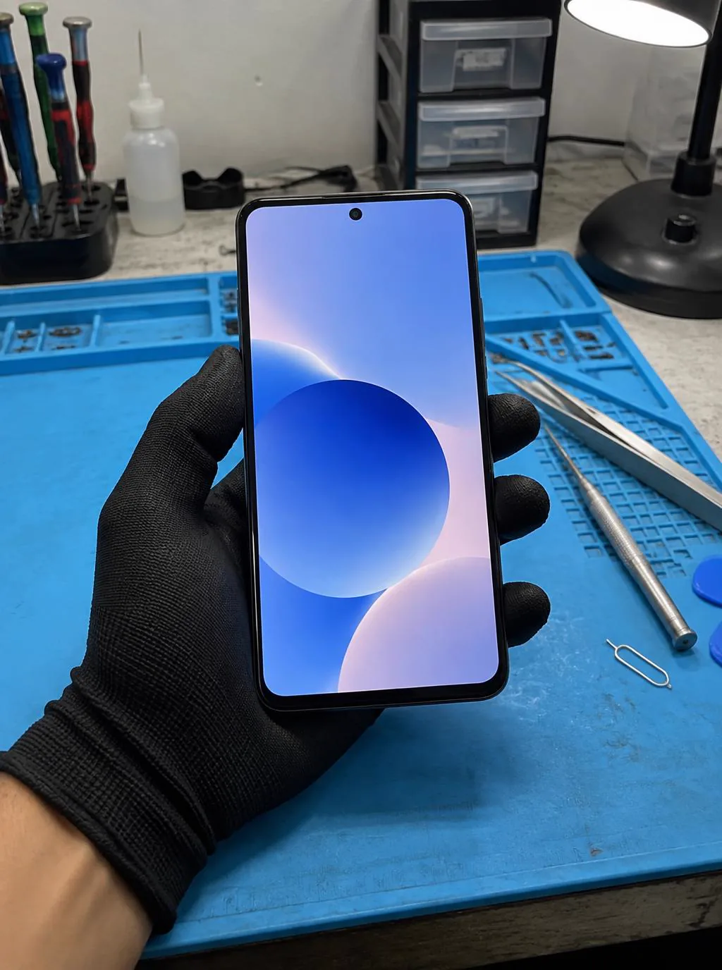Técnico com luva antiestática inspecionando um smartphone consertado sobre o tapete azul